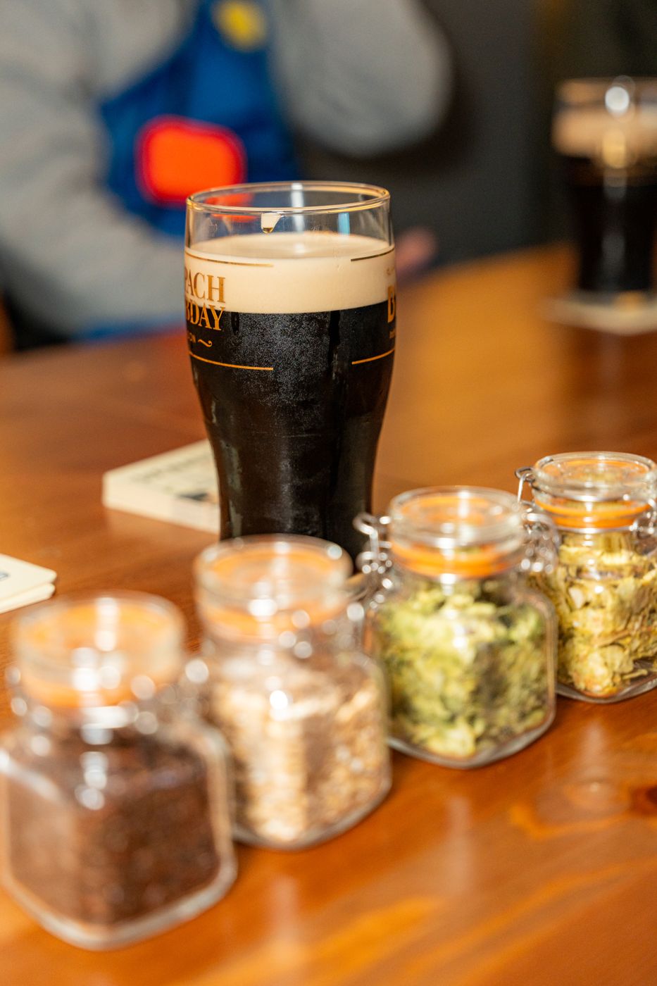 A stout alongside jars of malt and hops